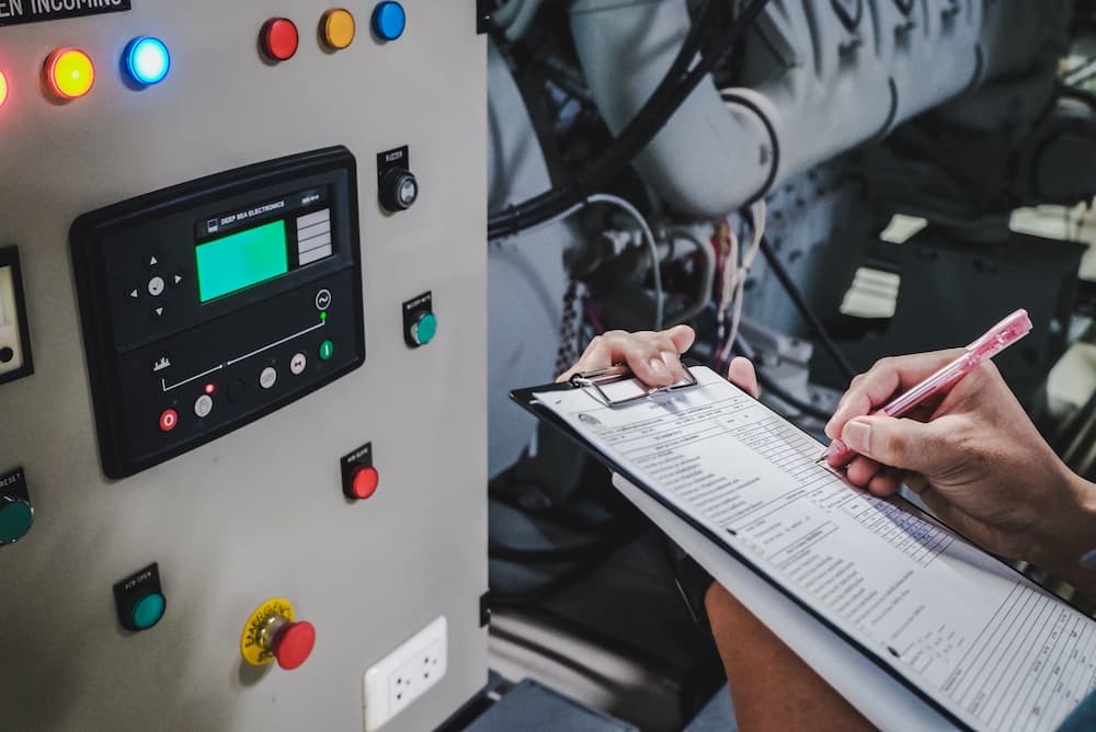 Person writing on clipboard in front of control panel.